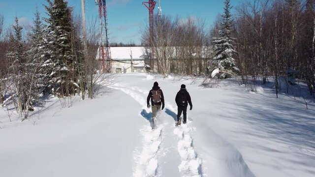Videography of two young documentary makers, walking steadfastly through deep snow, towards telecom towers base station on mountains.
