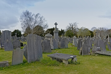 Spooky old decayed grave monuments with crosses in Glasnevin, green cemetery with bare trees in , Dublin, Ireland