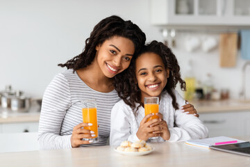 Cute black mother and daughter drinking orange juice with cookies