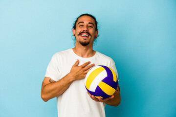 Young caucasian man with long hair isolated on blue background laughs out loudly keeping hand on chest.