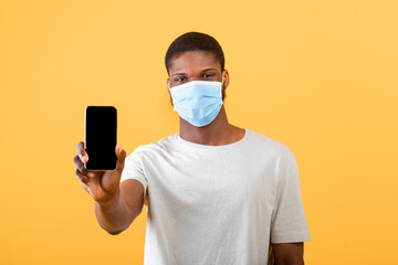 African american man in protective mask showing cellphone with blank screen to camera, space for your design