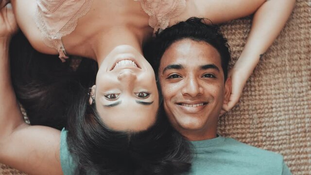 Young joyful people laying together with love and relationship at home - top view of young couple smile and enjoy life - boyfriend and girlfriend interracial portrait looking on camera from the ground