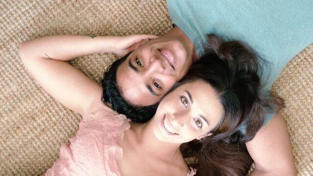 Happy young interracial couple viewed from above laying on the floor at home - cheerful black and caucasian boy and girl together smiling at the camera - new house owner and married lifestyle people
