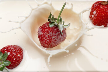 Ripe strawberries fall into the cream. Splashes of milk.
