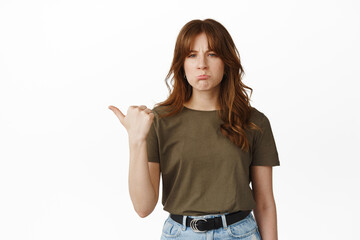 Sad and disappointed girl student pointing left, grimacing and sulking displeased, complaining on...