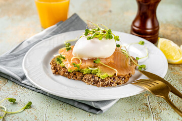 A home-made toast with mashed avocado, salmon, poached egg and microgreens in a plate. Healthy food concept. Omega 3 fats. Brain food