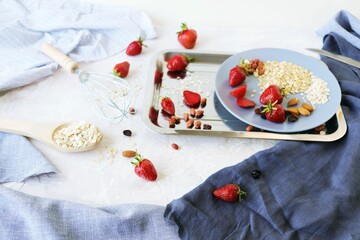 Healthy breakfast ingredients on the table, strawberries, oatmeal and nuts on a light background