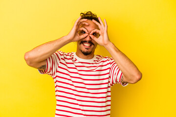 Young caucasian man with long hair isolated on yellow background showing okay sign over eyes