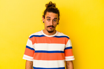 Young caucasian man with long hair isolated on yellow background sad, serious face, feeling...