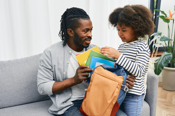 Father helps daughter to put color copybooks in school bag before a school day