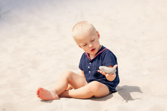 young  toddler boy kid playing in sea beach sand stone