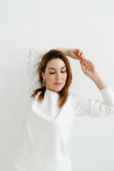 girl with red hair in a white sweater holds her hands above her head