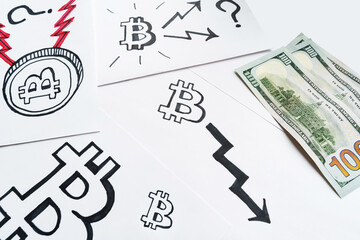 Drawn bitcoin icon with black arrow leading down, American dollars and other Bitcoin logos on the white background. Trends in bitcoin exchange rates and value of cryptocurrency.