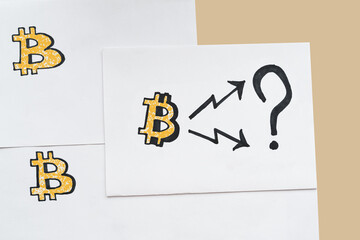 Three yellow symbols of Bitcoin are drawn on the sheets of paper with arrows leading to top and down. Rise and fall of bitcoin in future. .
