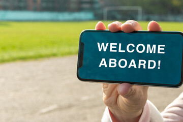 Welcome aboard message on the screen of the smartphone. Women's hand holds a smartphone and shows a message which invites a person to the team. Business concept.