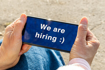 Woman holds a phone on which the message is written about the start of employment. We are hiring inscription on the screen of the smartphone. difficulties in the job search process.
