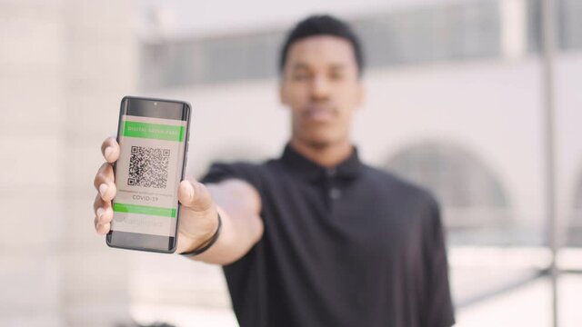 Young African American man showing his digital green pass. Certificate of immunity as proof of vaccination against covid 19. Ready to travel concept.
