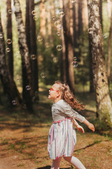 Little funny girl plays with soap bubbles in nature in summer