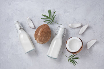 Fototapeta na wymiar Healthy flat lay concept. Vegan milk bottles, coconut slices and palm branch on gray background. Top view