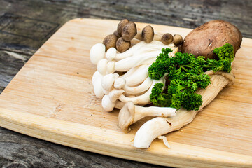 Mushrooms on a wooden cutting board with green parsley. Mushrooms ingredients for a mushroom soup on a wooden plank.