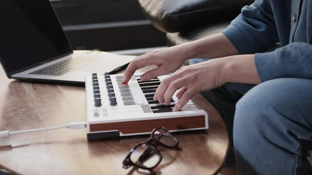 Woman hands playing on midi controller with buttons, producer of music with laptop on table. Closeup of hands playing on keys with pads, home studio with professional equipment