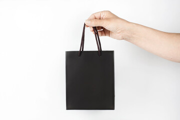 Dark paper bag with a handle in the hand of a woman on a light background, a woman holding a...