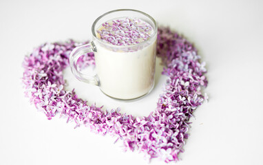Lilac flowers laid out in the shape of a heart and a cup of hot morning coffee in a glass cup on a white background. Copy space for text. Concept of holidays and good morning wishes.