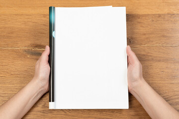Obraz premium Woman holding brochure with blank cover on wooden background, top view. Mock up for design