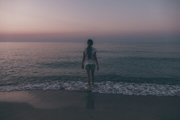 young woman, teenager girl, view from the back, goes into the dark blue sea, loneliness, determination, pink toned