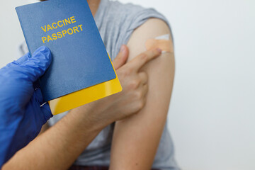 Coronavirus Vaccination passport concept. Hand in medical glove holding passport with covid-19 vaccine certificate on background of   man with coronavirus vaccine injection. Travel due Covid-19