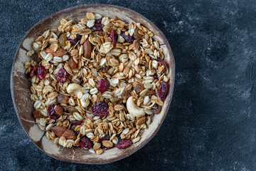 Granola with oatmeal, dried fruit, honey, raisins, dry cranberry, almond and cashew nuts in a coconut bowl, close up