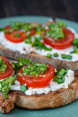 Delicious toasted bread with white cream cheese, green wild garlic and tomato on plate, close up