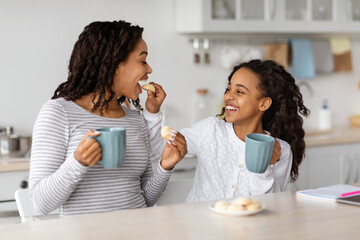 Laughing black girl feeding her mom with cookies