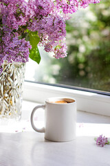 A bouquet of flowers on the window and coffee in a white cup in the rays of sunlight. A bouquet of lilacs and a cup of coffee. - 436735905