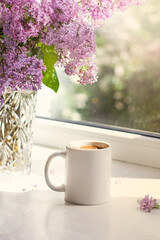 A bouquet of flowers on the window and coffee in a white cup in the rays of sunlight. A bouquet of lilacs and a cup of coffee. - 436735919