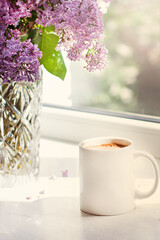 A bouquet of flowers on the window and coffee in a white cup in the rays of sunlight. A bouquet of lilacs and a cup of coffee. - 436735942