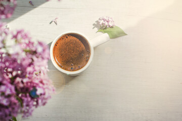 A bouquet of flowers on the window and coffee in a white cup in the rays of sunlight. A bouquet of lilacs and a cup of coffee. - 436735970