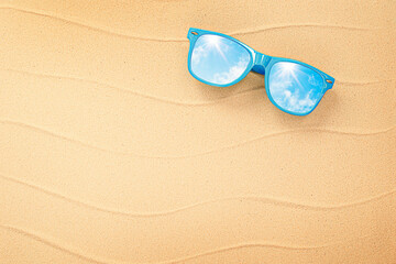 Fototapeta na wymiar one sunglasses with a reflection of the sky lying on the sea sand