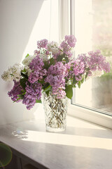 Vase with a bouquet of lilacs on the window.