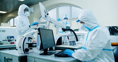 Mixed-race medical scientists wearing protective uniforms, masks and face shields working in modern...