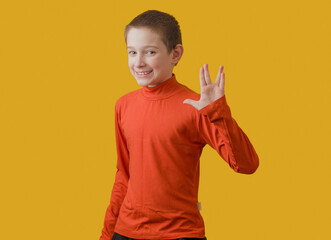 boy in orange turtleneck showing vulcan salute sign, posing on yellow background