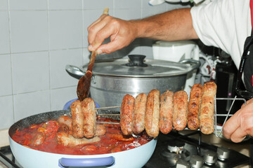 a man cooking sausages with tomato sauce
