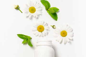 Herbal medicine concept. White plastic bottle for pills or tablets with fresh chamomile flowers and mint leaves on white background.  © Iryna