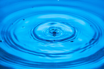 Macro view of drops making circles on blue water surface isolated on background.