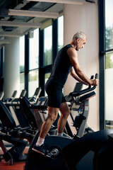 Fototapeta na wymiar Full length of mature athletic man using exercise bike while working out in a gym.