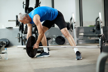 Fototapeta na wymiar Mature sportsman adjusting weight disk on barbell during gym workout.