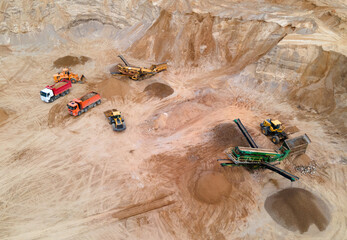 Wheel loader loading sand into dump truck in open pit. Arial view of jaw crusher sand making production line. Heavy mining machinery in quarry. Truck transports minerals from opencast. Soft focus