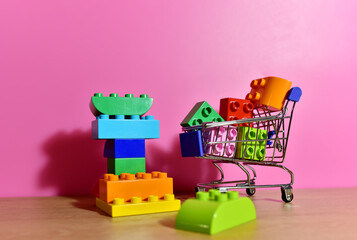 Obraz premium Toy plastic bricks in shopping cart for kids. Plastic construction blocks for children play. Colorful building block in basket trolley for buy. Recycling and reuse of plastic, shopping and delivery