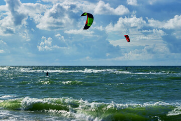 Two kite surfers glide on the sea in sunny windy weather