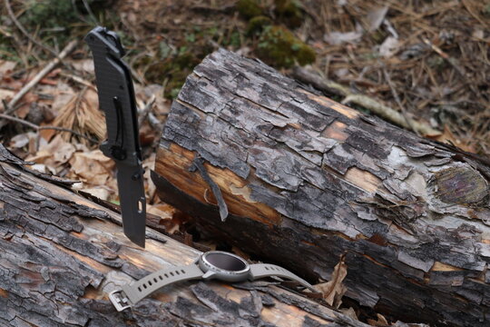 Folding knife and and smart watch on a tree log in the forest. Rest and hiking. Gadgets in nature.